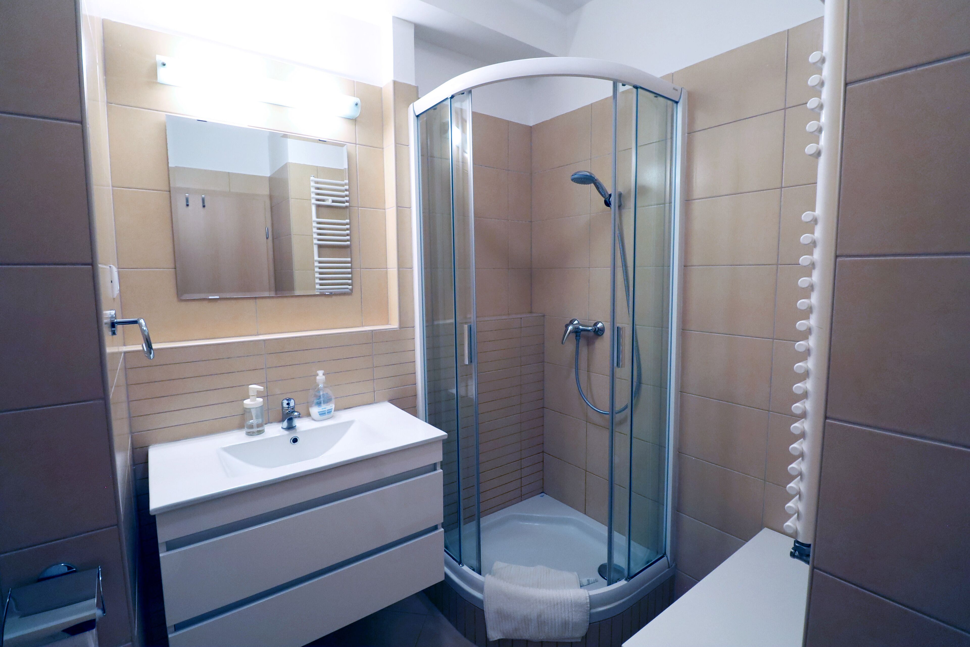 Un bagno moderno con cabina doccia in vetro, lavabo bianco e specchio sopra il mobile.