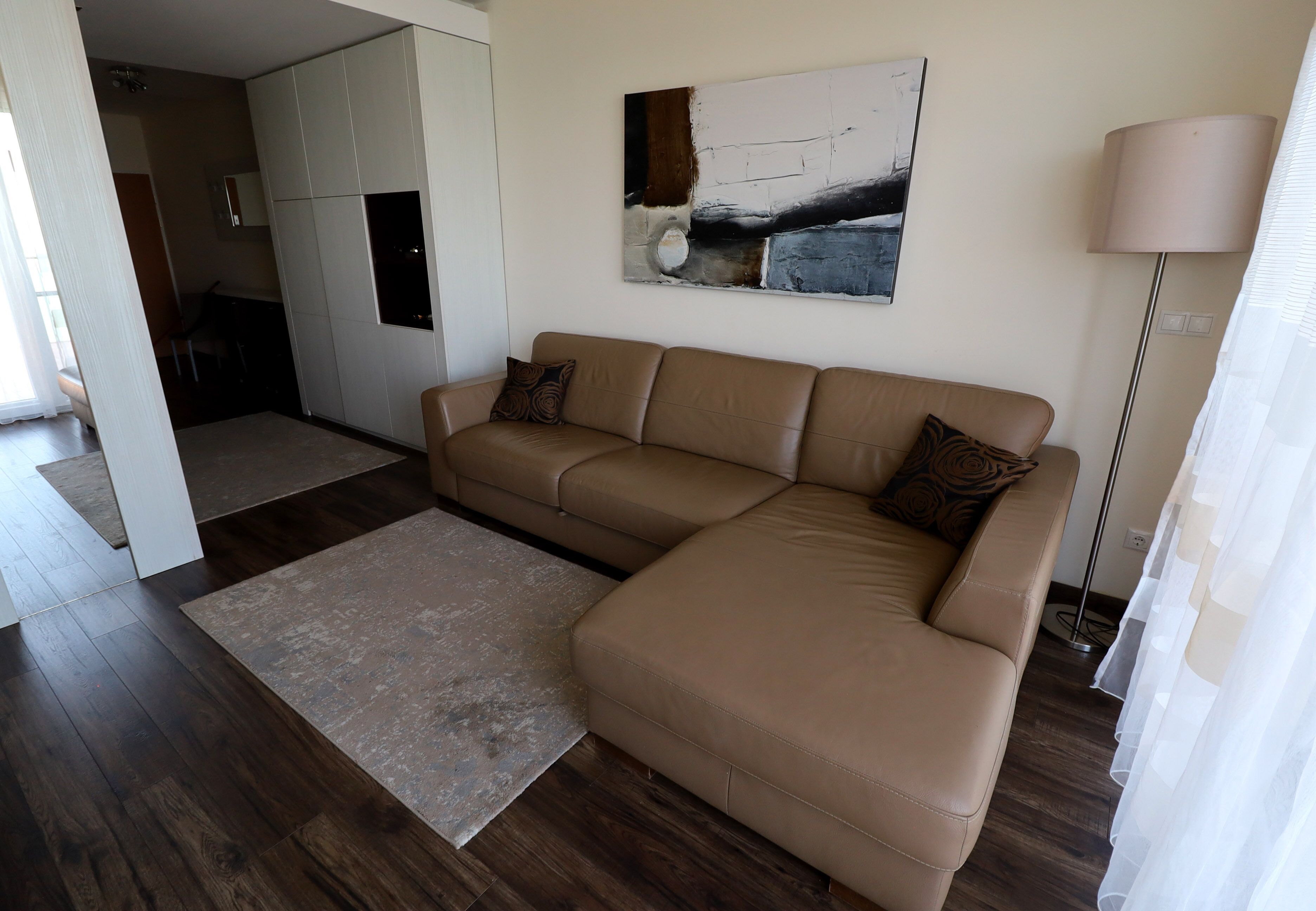 A modern living room with a large L-shaped beige sofa, a small rug, and a contemporary abstract painting on the wall.