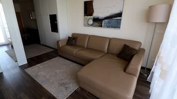 A modern living room with a large L-shaped beige sofa, a small rug, and a contemporary abstract painting on the wall.