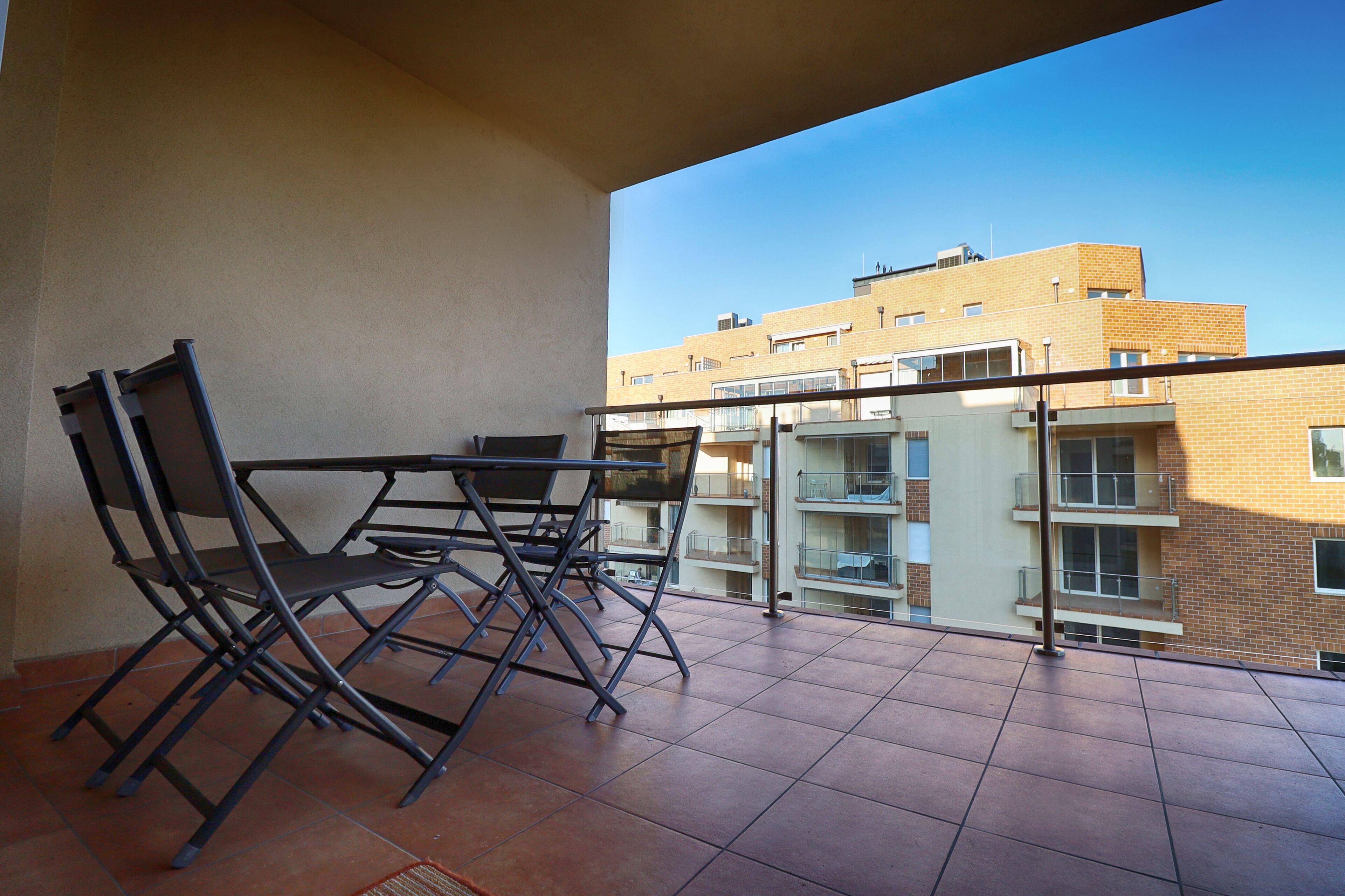 Un balcón con mesa y sillas, con vistas a un edificio con varios balcones.