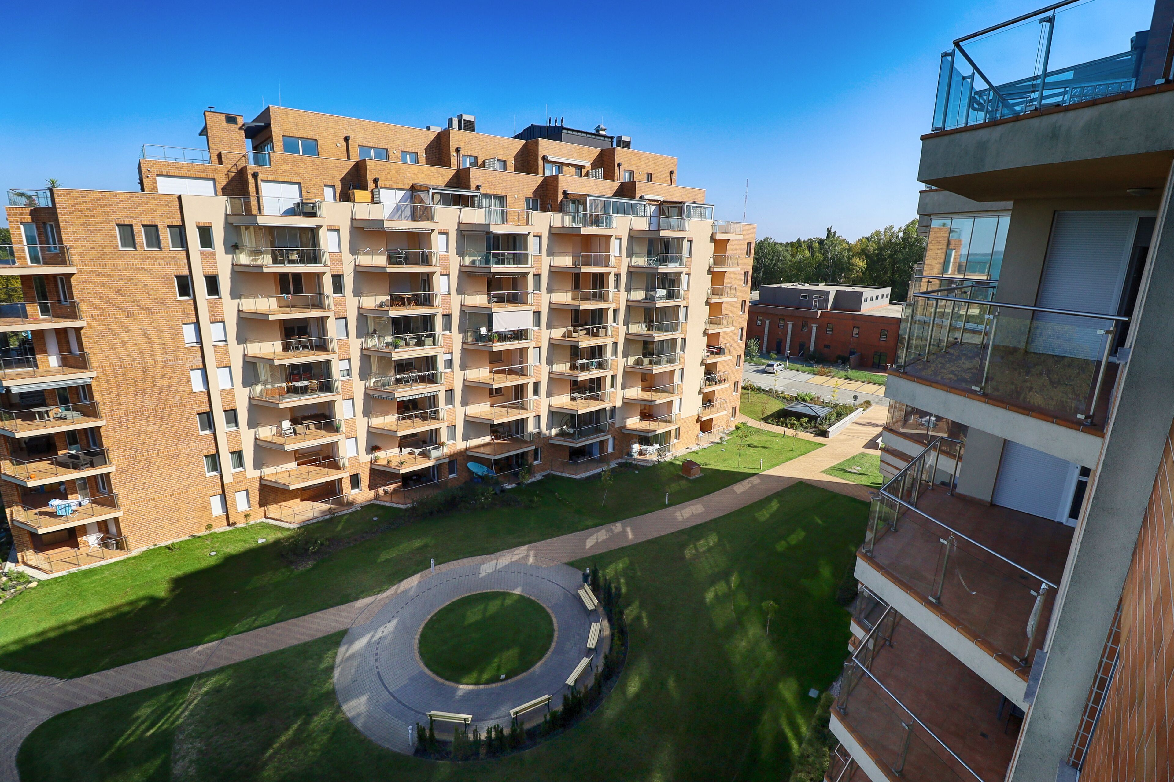 A multi-story residential building with balconies, a circular driveway, and a grassy area.