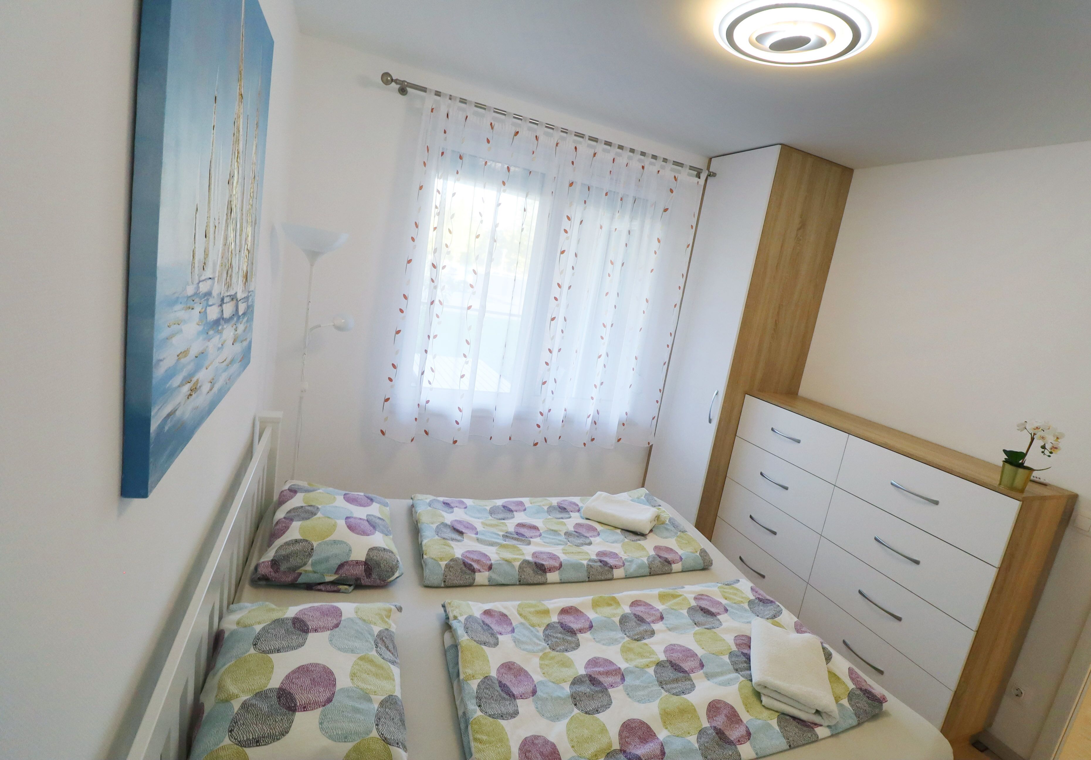 Un dormitorio con dos camas, un cuadro en la pared, una ventana con cortinas y un mueble de madera con cajones.