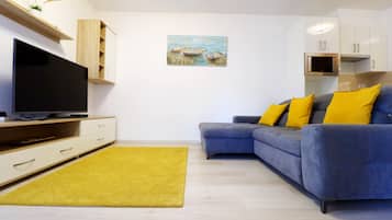 A modern living room with a flat-screen TV, a sofa with yellow cushions, and a painting on the wall.