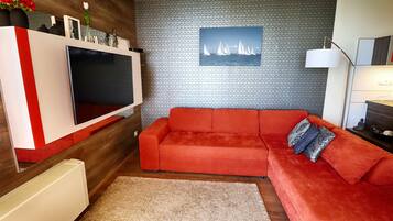 Una sala de estar moderna con un sofá rojo, un televisor de pantalla plana, un papel tapiz estampado y un cuadro con barcos de vela.