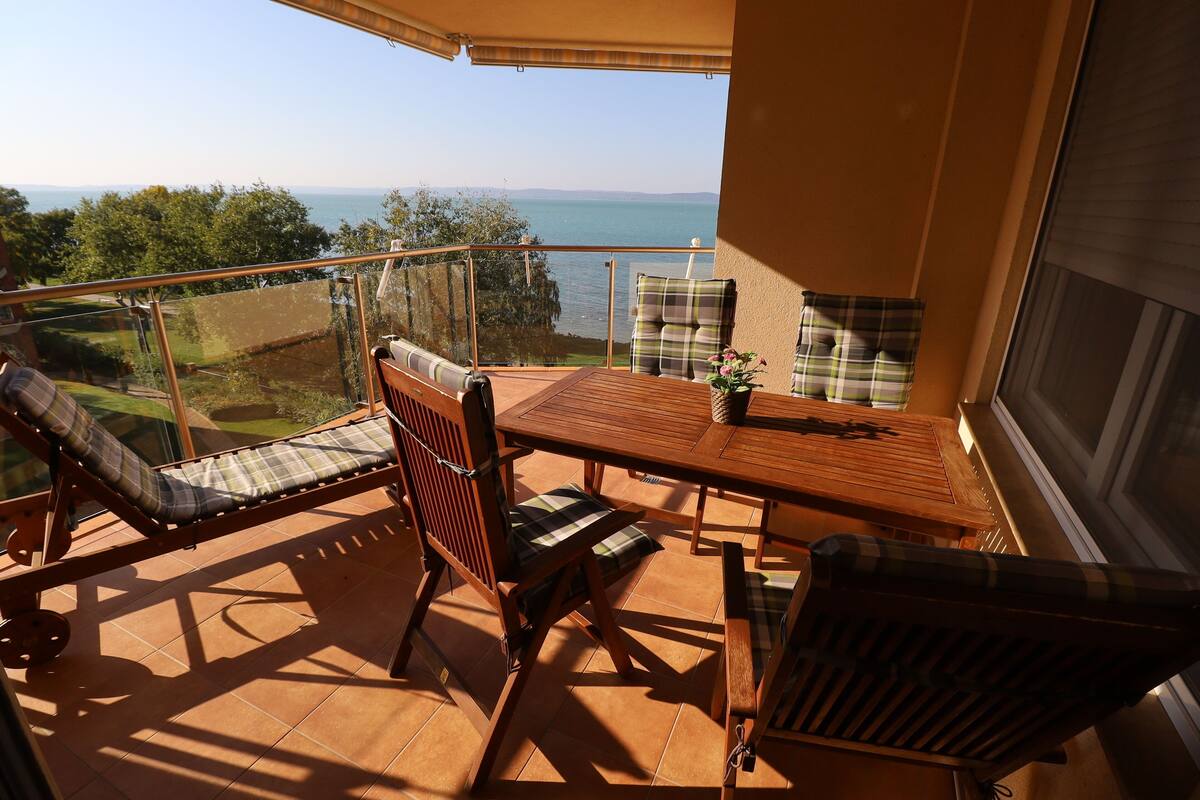Ein Balkon mit Holztisch und -stühlen, einer Glastrennwand und Blick auf das Meer.