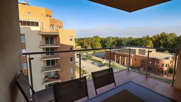 A balcony with two chairs, a table, and a view of a parking lot and buildings.