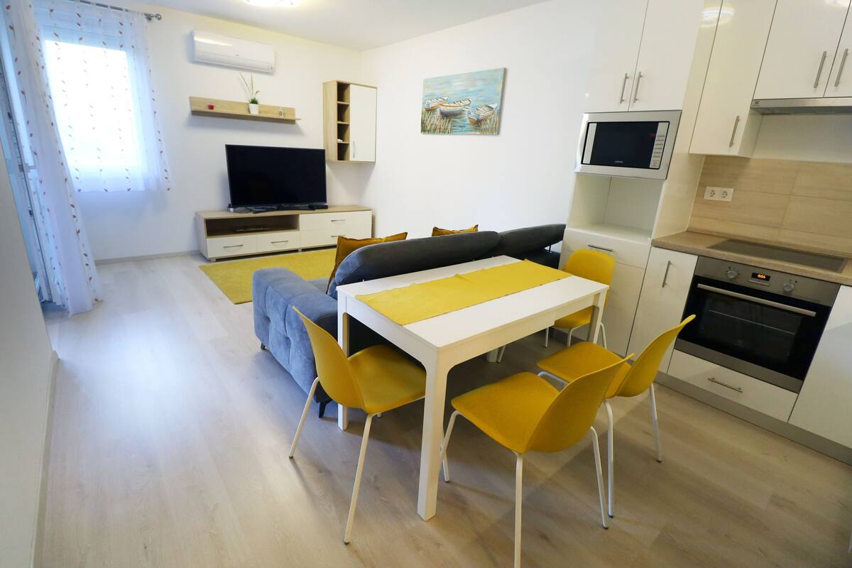 Ein modernes Wohnzimmer mit einer Couch, einem Fernseher und einem Esstisch mit gelben Stühlen.