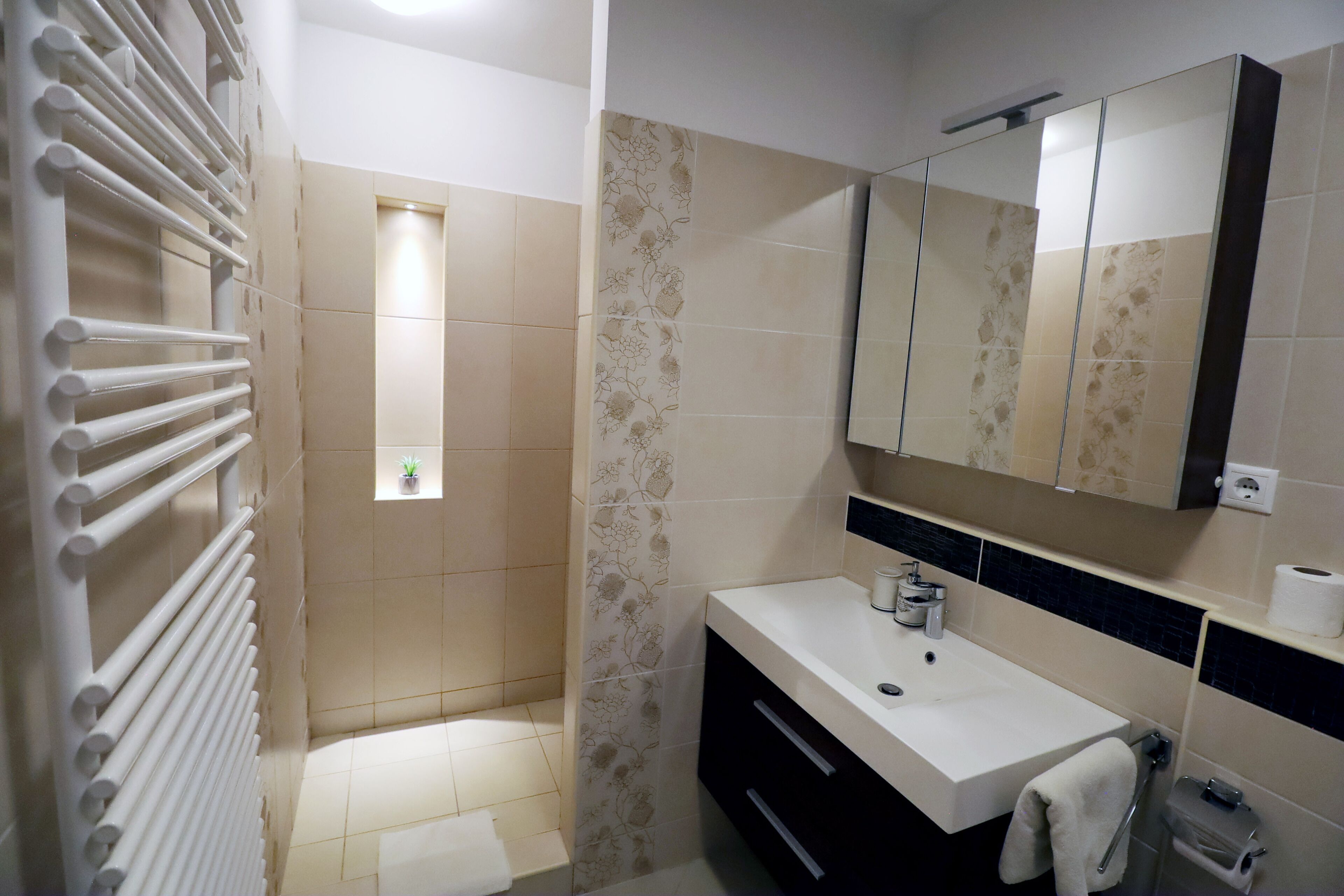 Un baño moderno con un lavamanos blanco, muebles oscuros, un espejo grande y una zona de ducha.