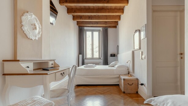 Un dormitorio con techo de madera, cama con ropa de cama blanca, escritorio con silla y ventana con cortinas.
