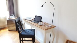 Une petite pièce bien éclairée, avec un bureau en bois, un ordinateur portable, une chaise et un radiateur.
