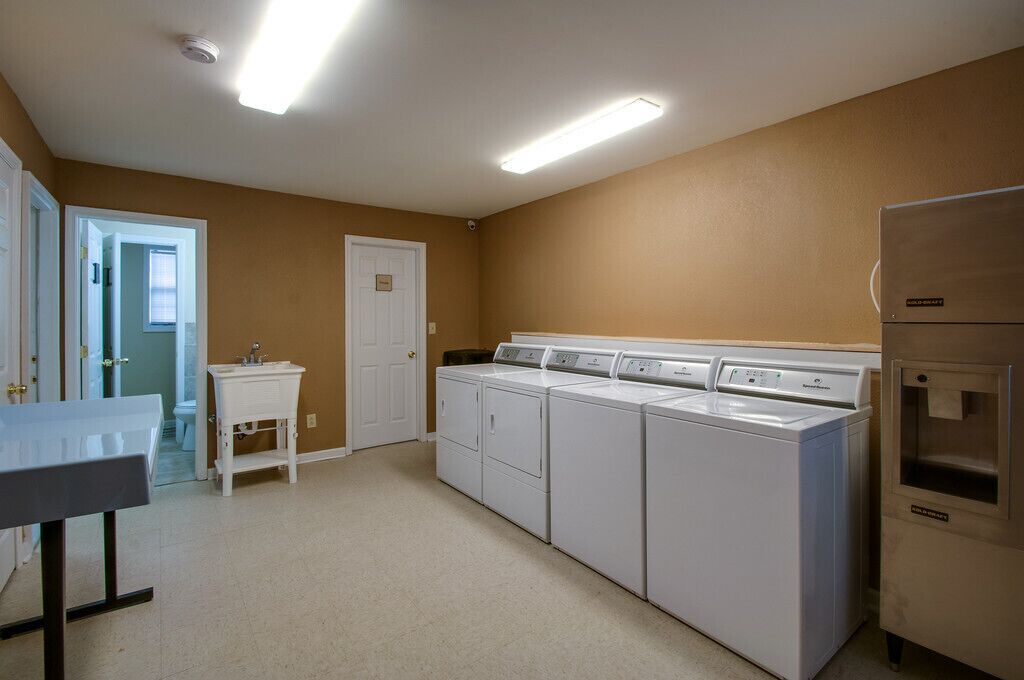 Un lavadero con cuatro lavadoras y secadoras apiladas, un lavamanos y una puerta que da a otra habitación.