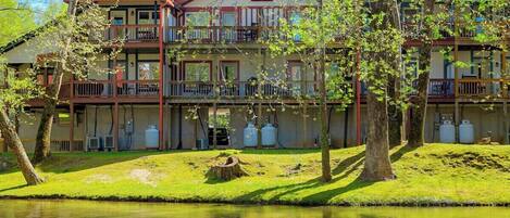 A multi-story building with balconies, a pond in front, and trees.