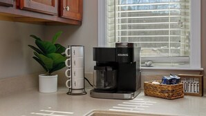 A coffee maker, a potted plant, a coffee pod holder, and a basket with coffee packets on a kitchen counter. - RiverHaus on Edelweiss - Cozy River Condo Downtown (Helen)
