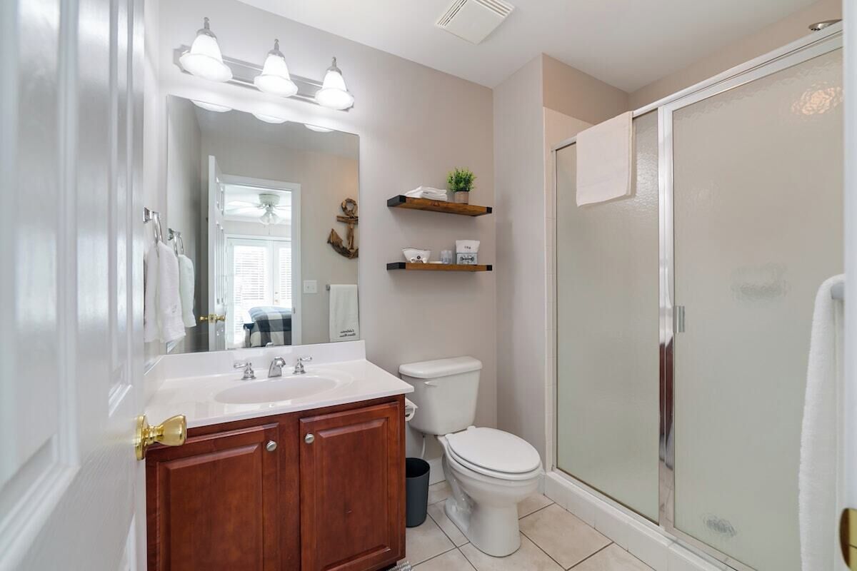 A bathroom with a white sink, wooden vanity, a toilet, and a glass-enclosed shower.