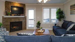 A living room with a fireplace, a television, a ceiling fan, and a sofa. - RiverHaus on Edelweiss - Cozy River Condo Downtown (Helen)