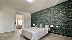 Een slaapkamer met een bed, een nachtkastje, een lamp en behang met een patroon.