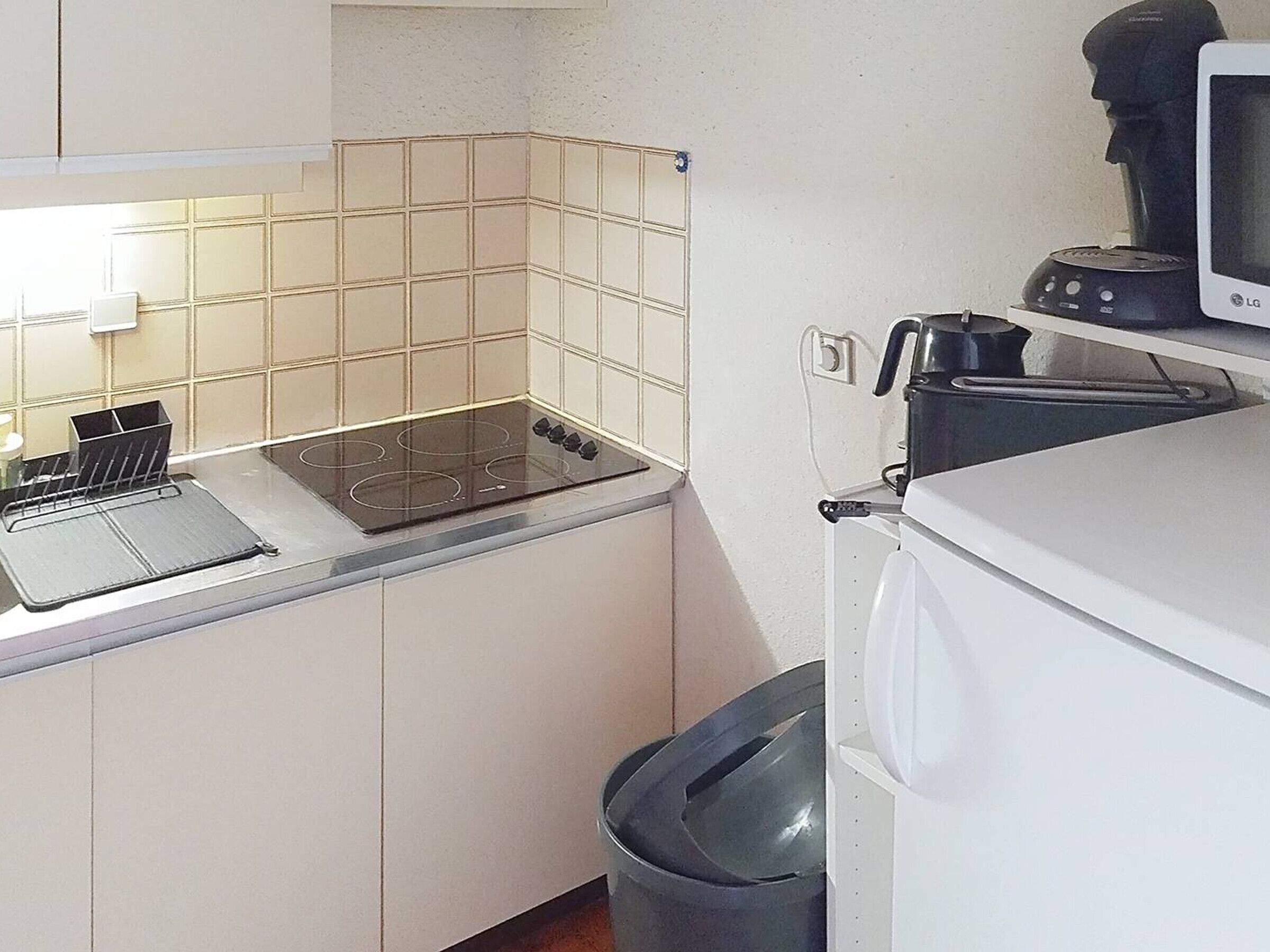 Uma cozinha compacta com fogão, cafeteira e lixeira.