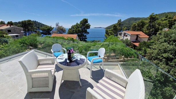 A terrace with wicker furniture, a table with a bottle and glasses, and a view of the sea and hills. - Apartment Coraline on Korcula, seafront (Smokvica)