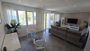 A modern living room with a sofa, chairs, a TV, and large windows offering a view of the outdoors. - Apartment Coraline on Korcula, seafront (Smokvica)