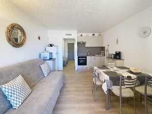 Een kleine woonruimte met kitchenette, eethoek en een slaapbank.