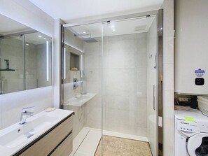 Une salle de bain moderne dotée d’une douche à parois de verre, d’un lavabo avec miroir et de toilettes équipées d’un distributeur de la marque Candy.