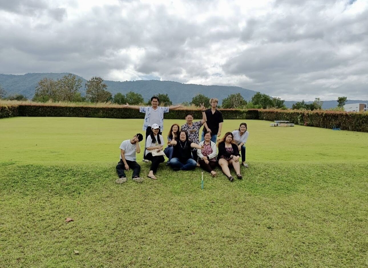 A group of people posing in a grassy outdoor area with a mountainous backdrop.