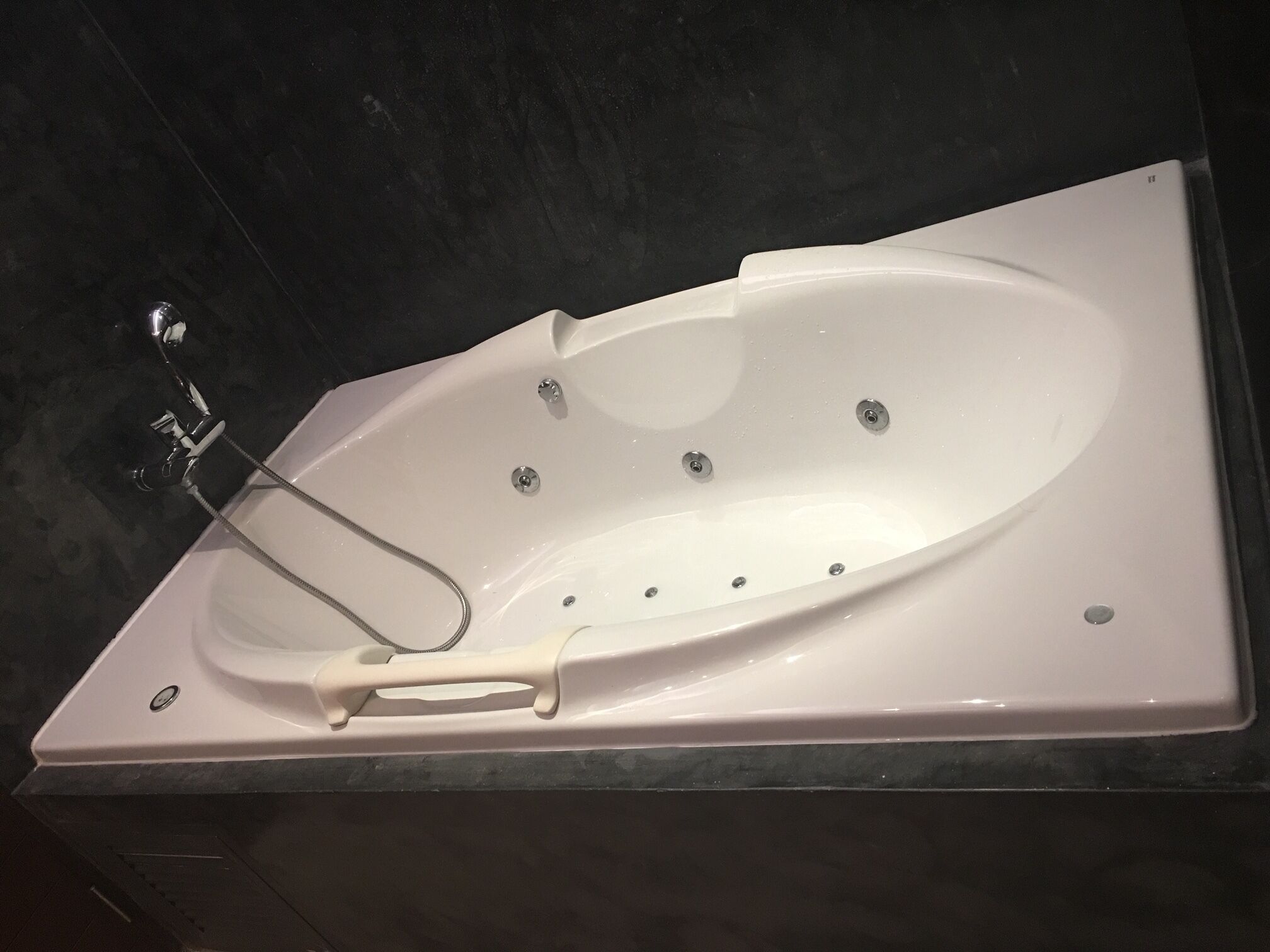 Une baignoire blanche autoportante, dotée d’un pommeau de douche à main, placée sur un plan de travail de couleur sombre.
