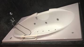 Une baignoire blanche autoportante, dotée d’un pommeau de douche à main, placée sur un plan de travail de couleur sombre.