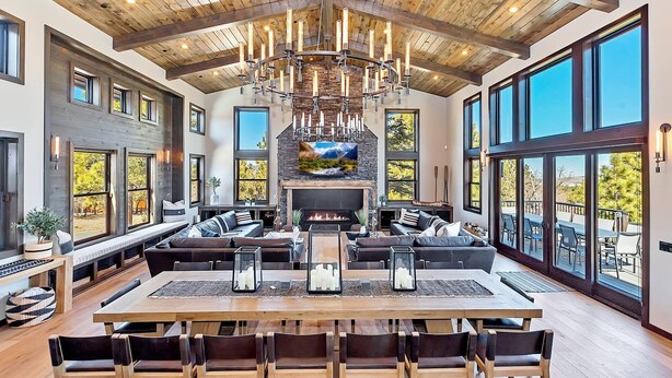 A spacious living room with a fireplace, large windows, and a high ceiling with exposed beams.