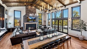 A spacious living area with a stone fireplace, large windows, and a high ceiling with wooden beams.