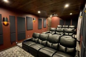 A home theater room with multiple black leather recliners, wall-mounted speakers, and a patterned carpet.