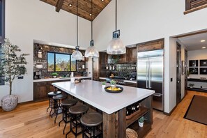 A modern kitchen with a large island, bar stools, pendant lighting, and a view of the outdoors.