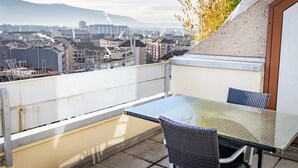 A balcony with a glass table and wicker chairs, overlooking a cityscape with buildings and mountains in the distance. - Starling Hotel Residence Genève (Geneva)