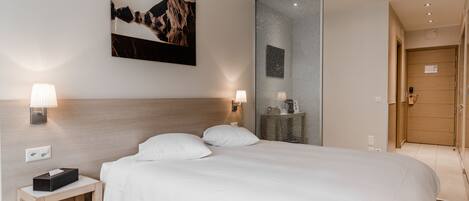 Una habitación de hotel moderna con una cama grande, lámparas de noche, una mesita de noche, un cuadro colgado en la pared y un espejo.