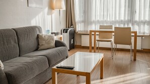 A modern living room with a sofa, a coffee table, a lamp, and a dining area with a chair and table. - Starling Hotel Residence Genève (Geneva)