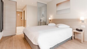 A modern hotel room with a large bed, a bedside table, a nightstand, a wall-mounted lamp, and a door leading to another room. - Starling Hotel Residence Genève (Geneva)