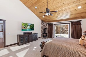 A bedroom with a large bed, a television on the wall, a fireplace, and a sliding glass door leading to an outdoor area. - Tranquility Lodge by Destination Big Bear : Luxury in Castle Glen Estates! Pool Table! (Big Bear Lake)