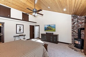 A spacious room with a large bed, a fireplace, a ceiling fan, and a painting on the wall.