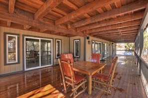 An outdoor wooden deck with a dining table and chairs, surrounded by glass doors and windows.