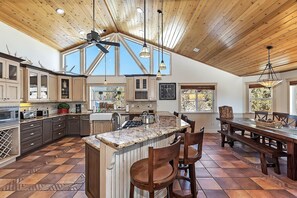 A spacious kitchen with a high ceiling, large windows, and a central island with bar stools.