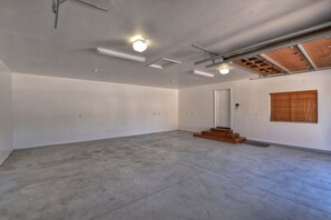 A spacious room with a concrete floor, a wooden staircase, and a door leading to another area. - Tranquility Lodge by Destination Big Bear : Luxury in Castle Glen Estates! Pool Table! (Big Bear Lake)
