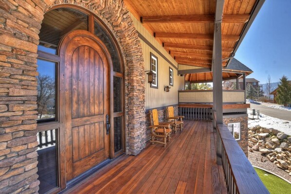 Un porche de madera con paredes de piedra, una puerta de madera grande y mobiliario exterior.