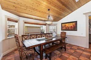 A dining area with a wooden table and chairs, a bench, a hanging light fixture, and a painting on the wall. - Tranquility Lodge by Destination Big Bear : Luxury in Castle Glen Estates! Pool Table! (Big Bear Lake)