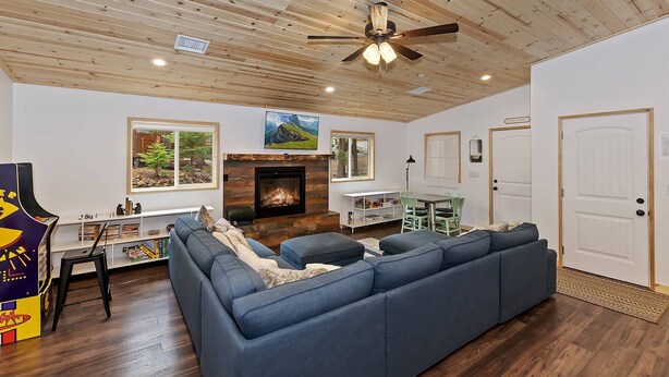 A living room with a blue sectional sofa, a fireplace, a ceiling fan, and a view of the outdoors through large windows.