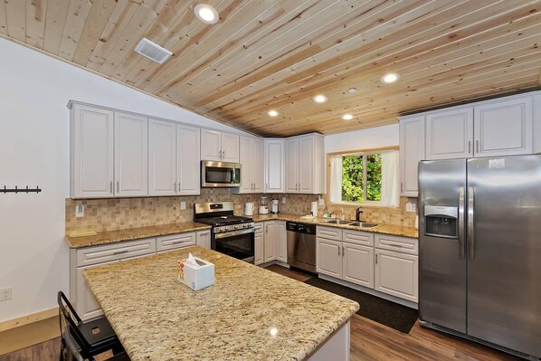 A modern kitchen with white cabinets, granite countertops, stainless steel appliances, and a wooden ceiling.