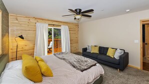 A bedroom with a bed, a sofa, a ceiling fan, and a window with curtains.