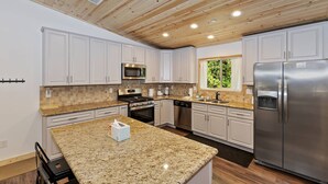 A modern kitchen with white cabinets, granite countertops, stainless steel appliances, and a wooden ceiling.