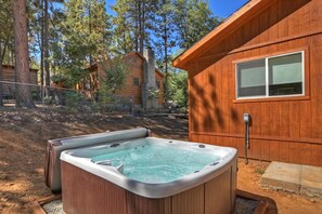A wooden cabin with a hot tub in a forested area.