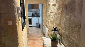 A narrow hallway with a tiled floor, a white table with a plant, and a kitchen visible in the background. - 'The Ucetia' appt in charming stone house in Uzès centre (Uzès)