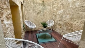 A small, enclosed outdoor patio with a wooden deck, two white wire-framed chairs, a small table with a potted plant, and a green mat. - 'The Ucetia' appt in charming stone house in Uzès centre (Uzès)